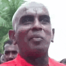 a man with a tattoo on his forehead is wearing a red shirt and looking at the camera .