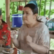 a woman is sitting at a table with a spoon in her hand and giving a thumbs up .