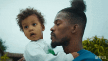 a man is holding a baby with a netflix logo on the bottom