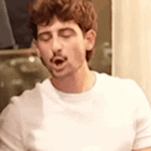 a man in a white t-shirt is yawning with his eyes closed and his mouth open .