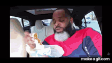 a man is sitting in the back seat of a car eating a sandwich .