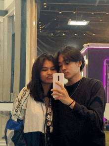 a man and a woman are taking a selfie in front of a mirror and the woman is wearing a jacket with kangaroo on it