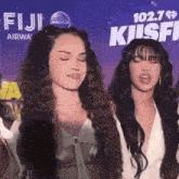 two women standing in front of a sign that says 102.7 fiji airway