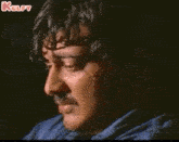a man with a mustache is crying with his mouth open in a dark room .
