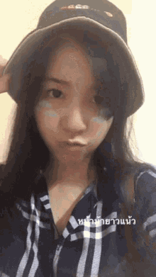 a woman wearing a hat and a plaid shirt is taking a selfie in thai