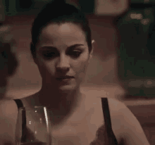 a woman is holding a glass of wine and looking at the camera .