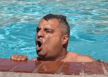 a man is yawning in a swimming pool while looking out of the water .