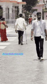 a man with a cane walks down a street with a woman in a red dress behind him