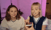 two girls are sitting in front of a sign that says " party @ 100k "