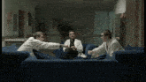 three men in lab coats are sitting on a blue couch and talking