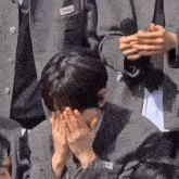 a man in a suit is covering his face with his hands while standing in a crowd .