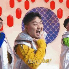 a man in a yellow jacket is laughing in front of a wall with red lanterns