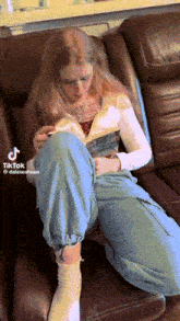 a woman sitting on a couch reading a book with a tik tok watermark