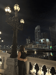 a woman stands on a bridge at night looking at the city skyline