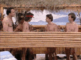 a group of naked men are standing next to each other behind a bamboo wall .