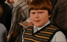 a young boy wearing a striped vest looks at the camera with a serious look on his face