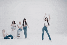 a group of women in white shirts and jeans are dancing in a white room
