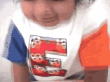 a young boy wearing a t-shirt with a picture of cars on it is crawling on the floor .