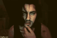 a man with long hair and a beard is looking at the camera with a serious look on his face .