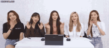 a group of girls are sitting at a table with a laptop and a tablet .