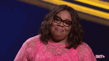 a woman wearing glasses and a pink lace top with the bet logo in the corner