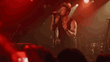 a man singing into a microphone in front of a crowd with a drum set behind him
