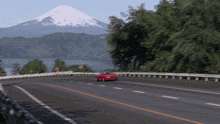 a red car is driving down a highway with a mountain in the background