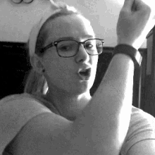 a woman wearing glasses and a headband is raising her fist in the air in a black and white photo .