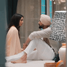 a man and a woman are sitting on a bed looking at each other .