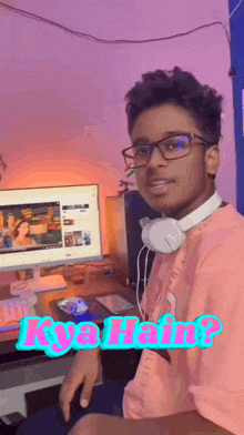 a boy wearing headphones and a pink shirt is sitting in front of a computer with the words kya hain written on the bottom