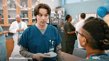 a man in a blue scrub is holding a plate of food and talking to a woman in a nbc ad