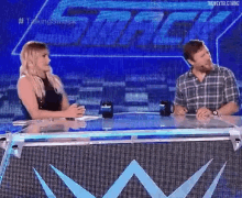 a man and a woman are sitting at a table in front of a large screen .