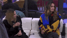 two women are sitting on a couch with a glass of wine