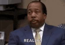 a man in a suit and tie is sitting at a desk and says `` really '' .