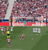 a soccer game is being played in front of a large mahou ad