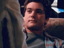 a man in a plaid shirt is sitting on a couch looking at something .