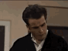 a man in a black jacket and white shirt is standing in a room and looking down .