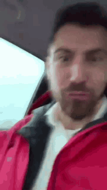 a man with a beard wearing a red jacket is sitting in a car