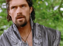 a man with a beard and curly hair is wearing a gray robe and earrings .