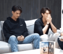 two men are sitting on a couch and one of them is covering his mouth with his hand .