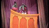 a cartoon eggplant and tomato are behind a wooden podium on a stage