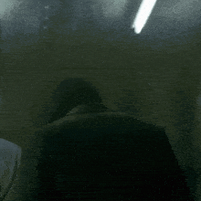 a man in a suit is sitting in a dark room looking out the window .