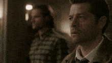 a man in a plaid shirt is standing in front of a window and looking down .