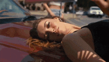 a woman is laying on the hood of a red car with her eyes closed .