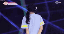 a girl in a blue shirt with yellow stripes is standing on a stage with her back to the camera .