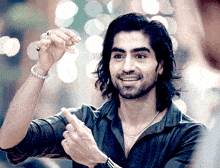 a man with long hair is smiling and holding a small object in his hand