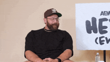 a man sitting in front of a sign that says " he 's crew "