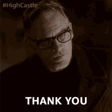 a man wearing glasses says " thank you " in a dark room