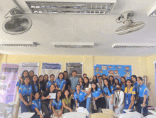 a group of people posing for a picture in a classroom with a poster on the wall that says ' filipino '