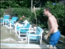 a shirtless man in blue shorts is standing next to a swimming pool